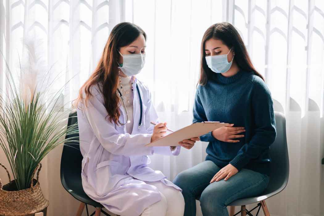 Doctor writing notes on a clipboard while consulting a female patient wearing a face mask