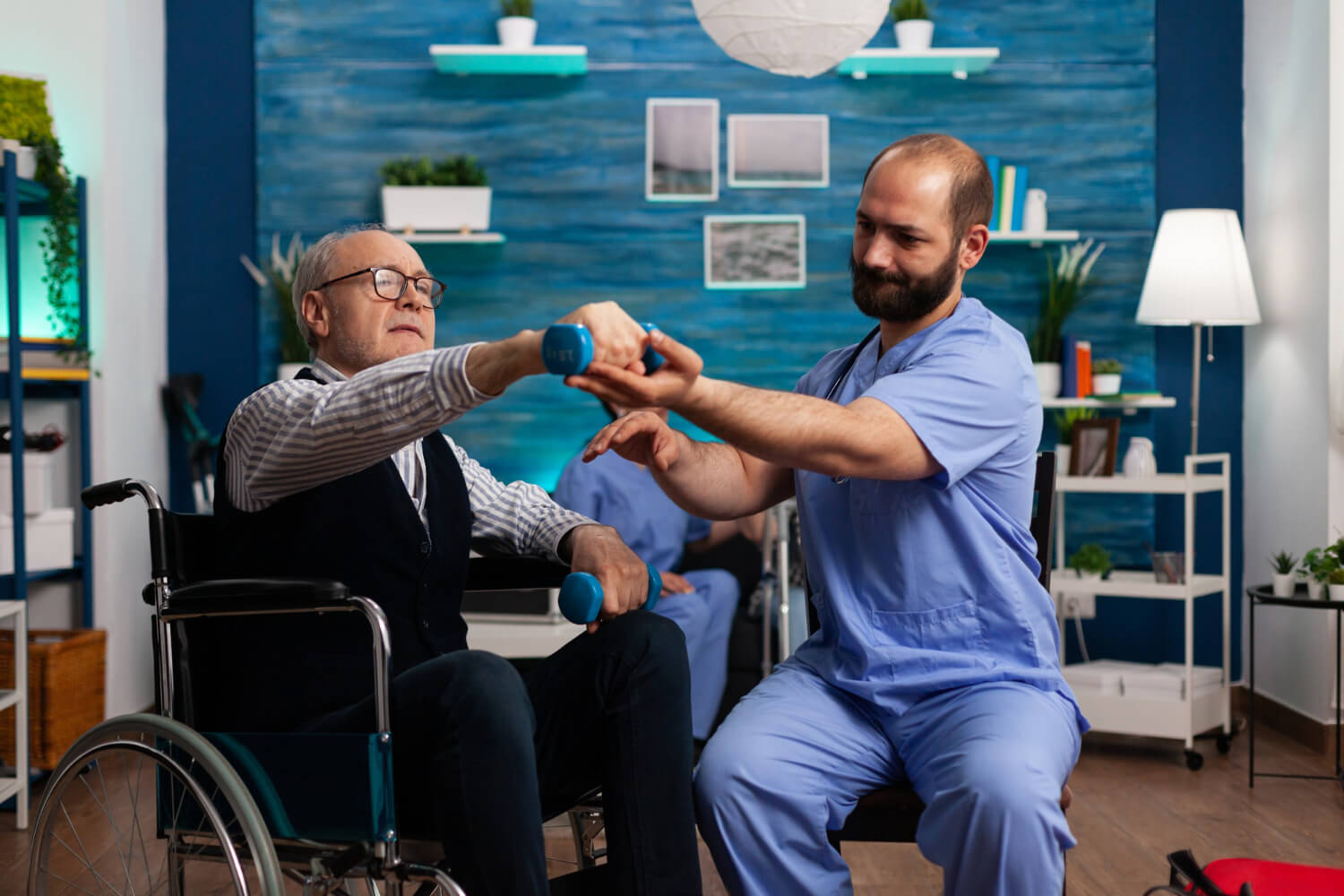 Physiotherapist assisting an elderly man in a wheelchair with arm strength exercises using dumbbells
