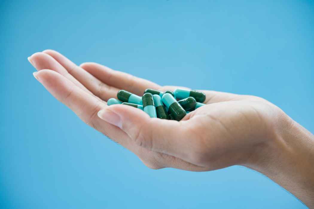 Hand holding green and blue capsules against a blue background