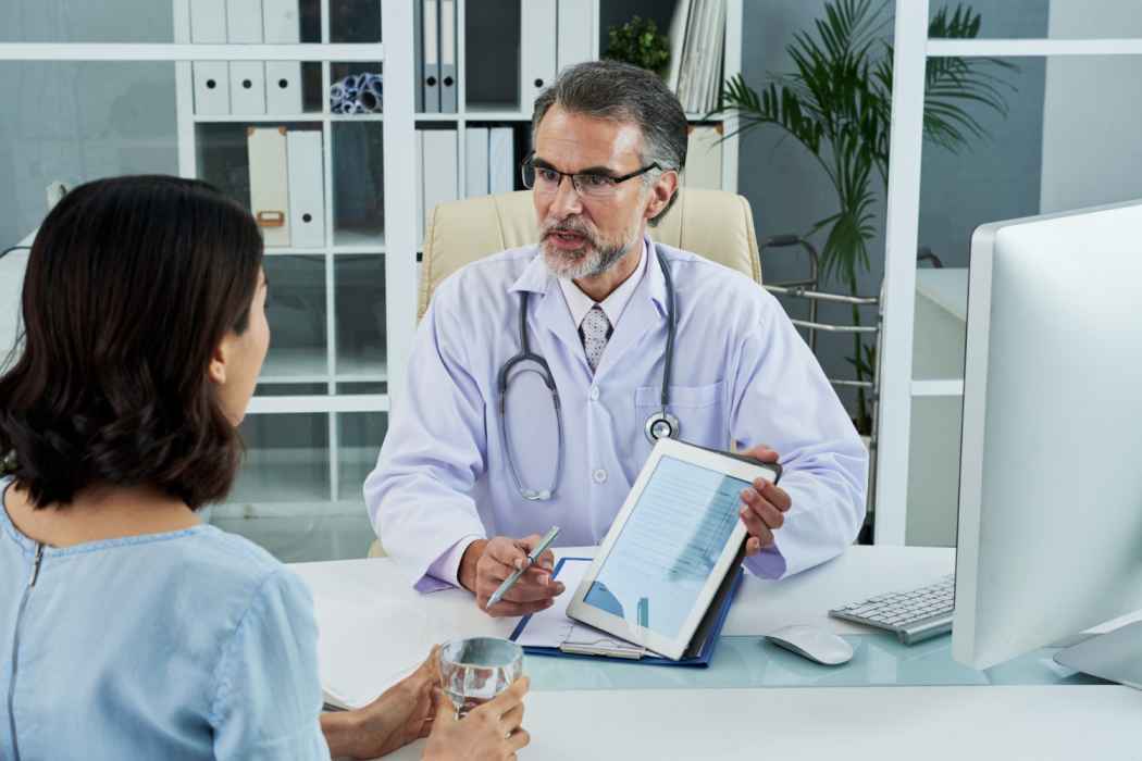 Doctor explaining medical test results to a patient using a digital tablet during consultation