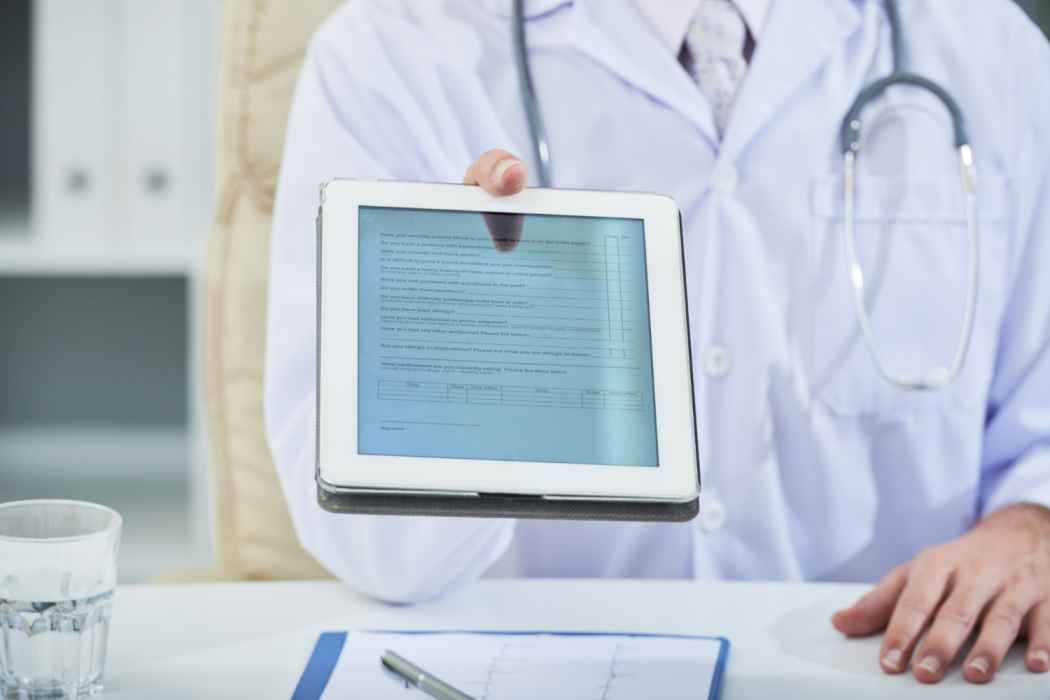 Doctor holding a tablet displaying a digital medical form during a patient consultation in a clinic.