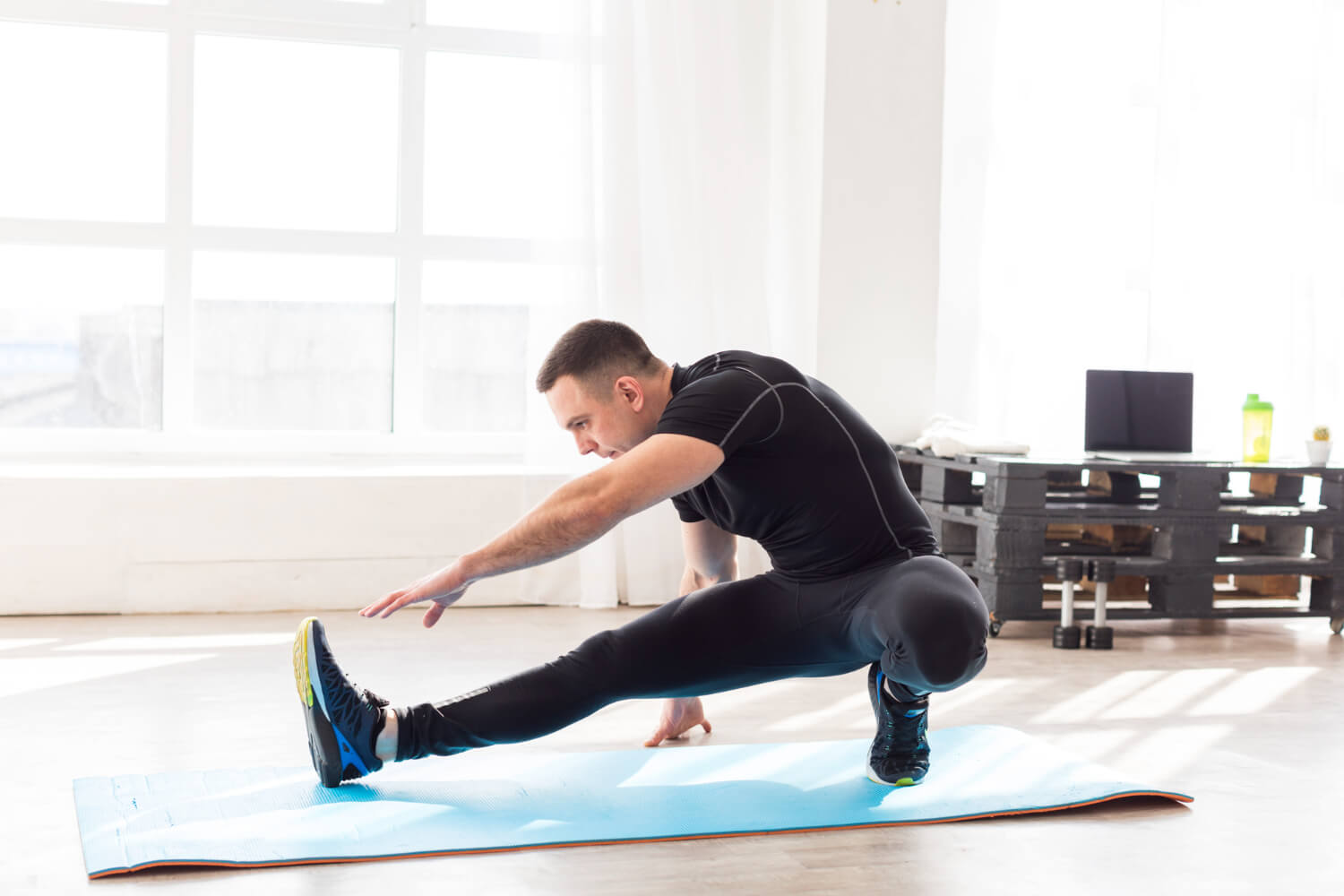 Man performing a deep lateral stretch exercise on a yoga mat in a fitness studio