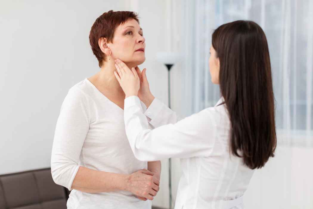 Doctor examining a middle-aged woman’s neck and throat during a medical checkup
