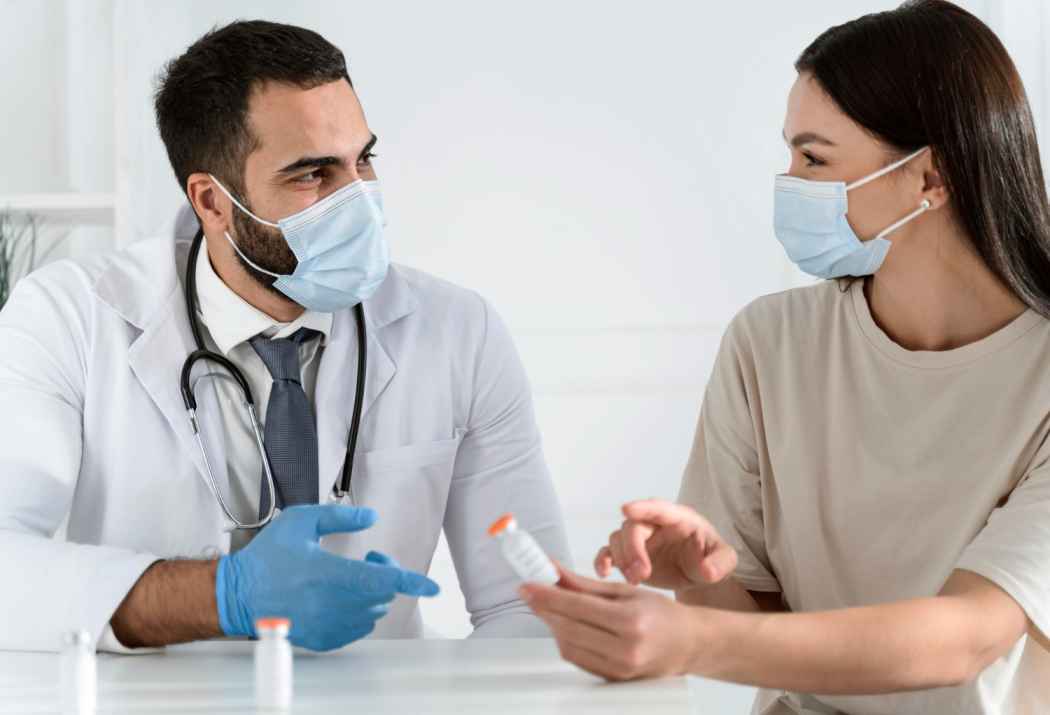 Doctor explaining medication usage to a female patient during a medical consultation while both wear face masks