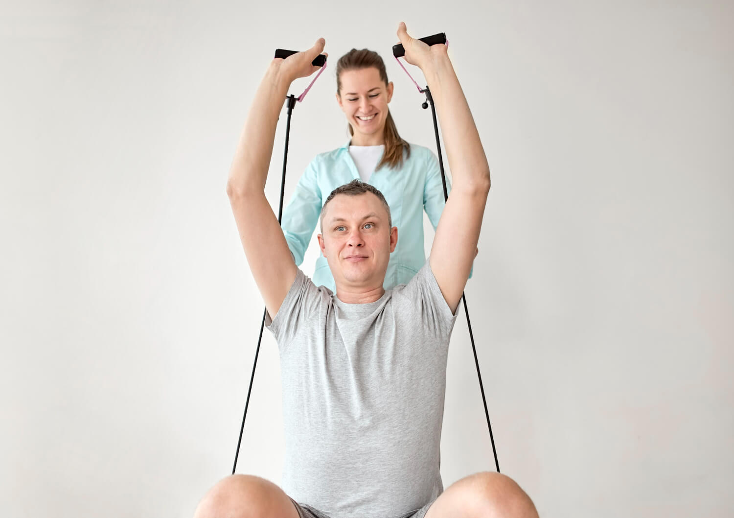 Physiotherapist supervising a male patient performing overhead resistance band exercises during rehabilitation