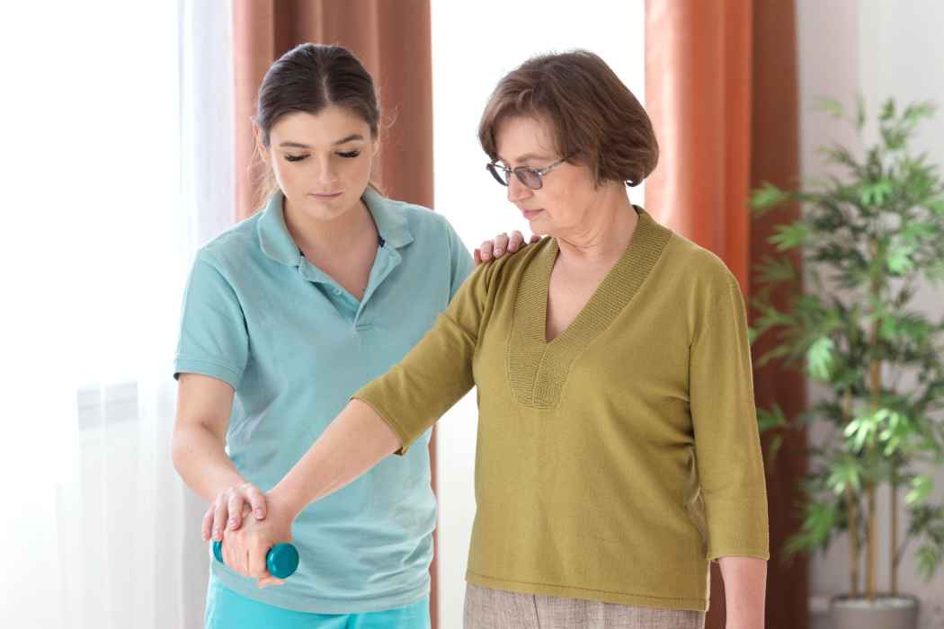 Physiotherapist assisting an elderly woman with arm exercise using a hand weight during rehabilitation