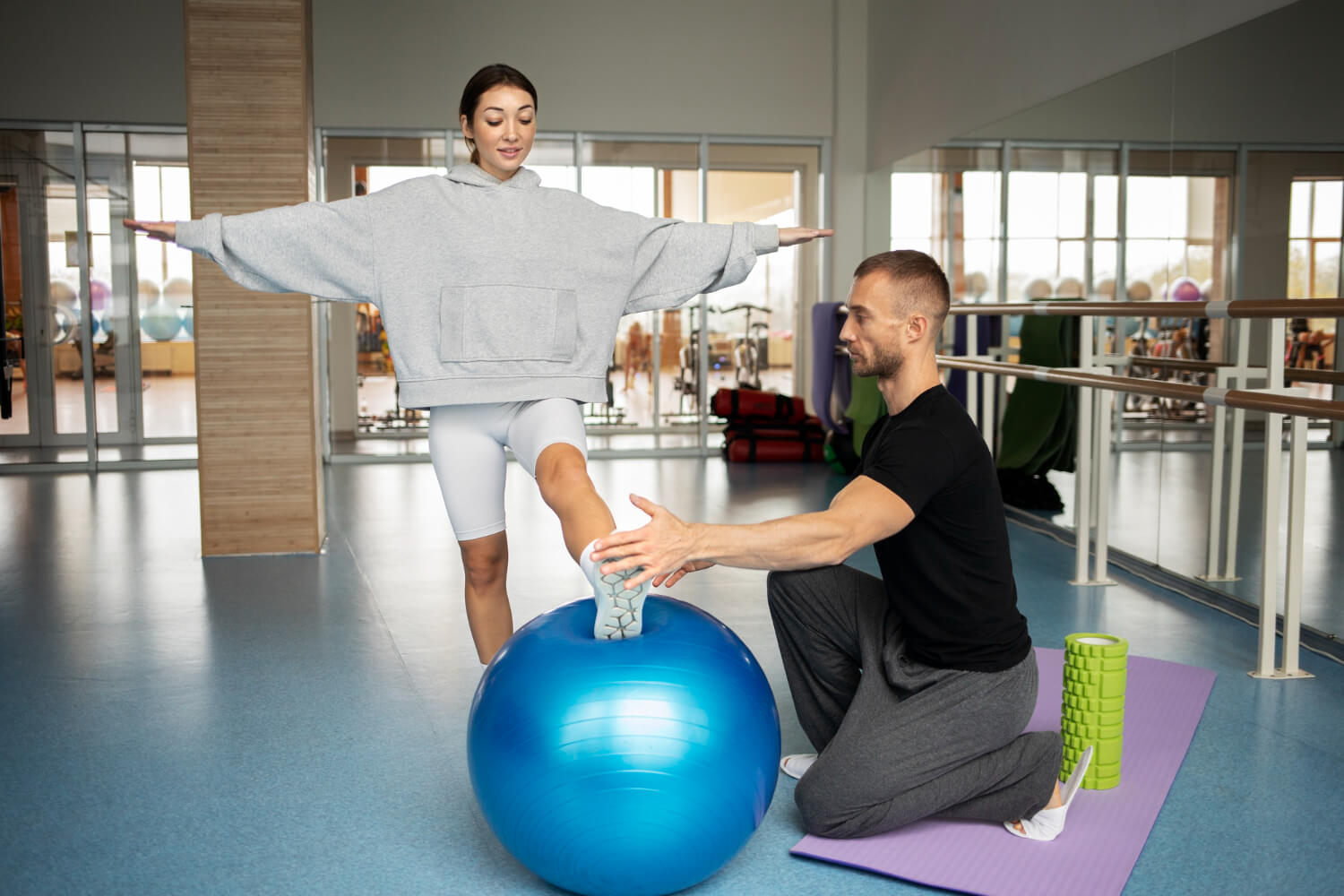 Physiotherapist assisting a woman with a balance exercise using a stability ball in a gym