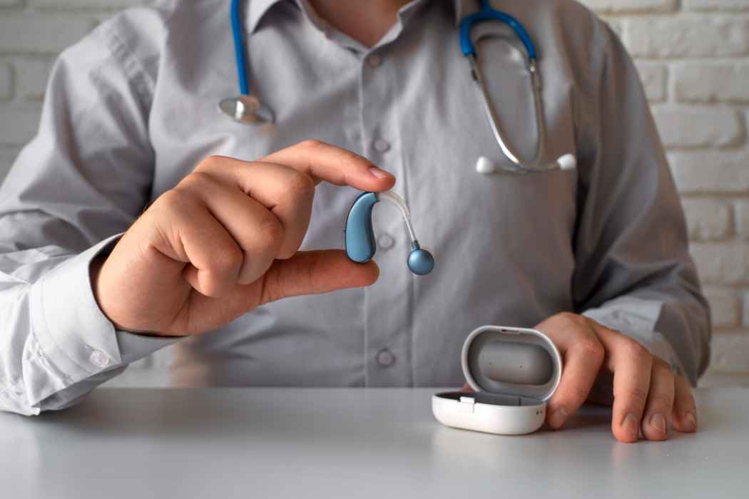 Doctor holding a modern hearing aid device with charging case in a clinic setting