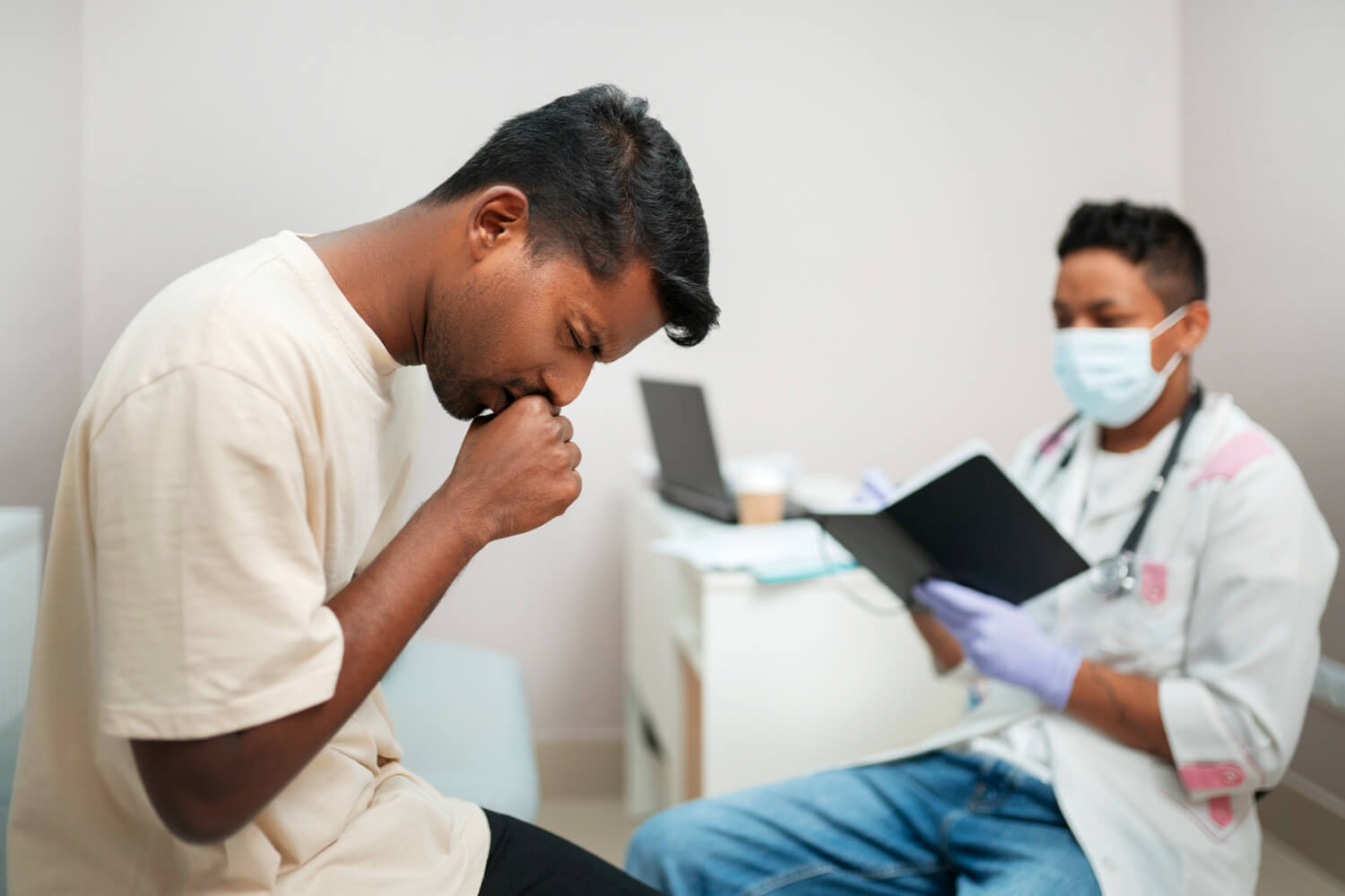 Man coughing during a medical consultation while a healthcare professional reviews patient notes