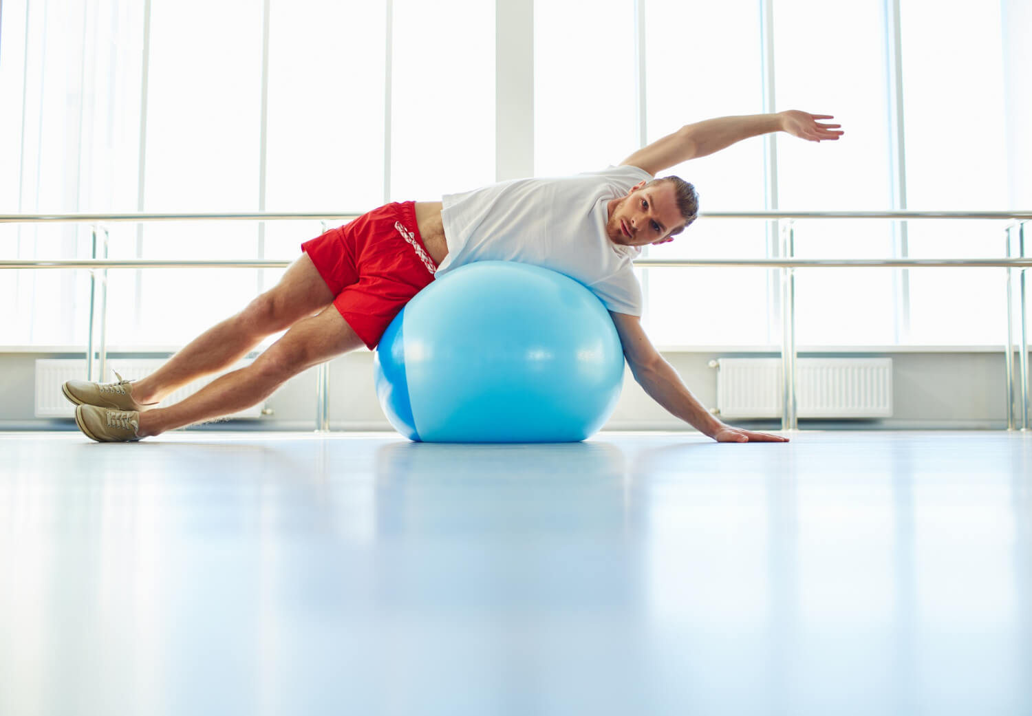 Man performing a side stretch exercise using a stability ball in a fitness studio
