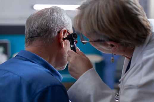 Doctor examining an elderly man’s ear using an otoscope during an ENT checkup