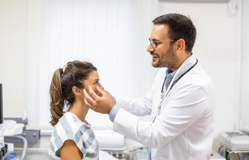Doctor examining a young woman’s eyes and face during a clinical checkup