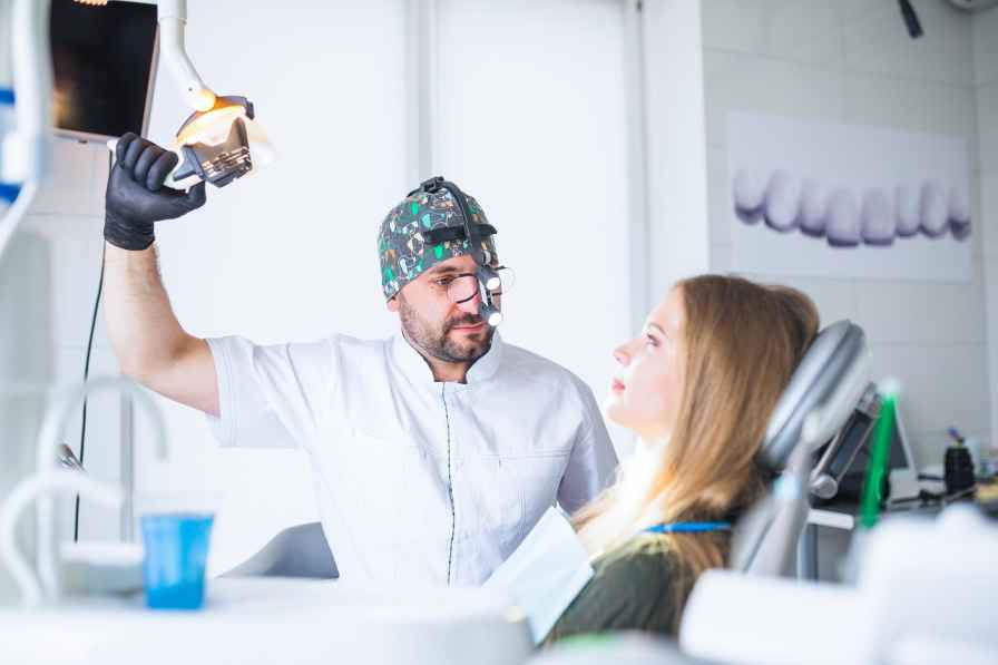 Dentist examining a patient’s mouth using a dental light and headlamp