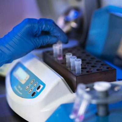 Gloved hand placing sample tubes into laboratory testing equipment