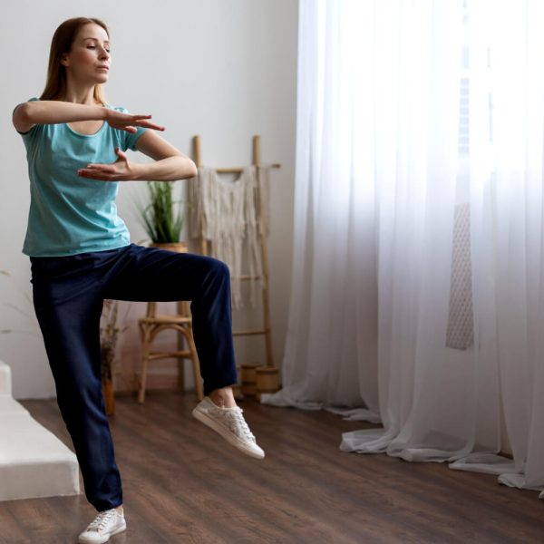 Woman performing a one-leg balance exercise indoors to improve stability and coordination