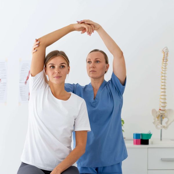 Physiotherapist assisting a female patient with an arm stretch during a rehabilitation session in a clinic